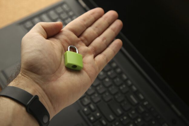 Eine Hand hält ein kleines, grünes Vorhängeschloss über einer Laptop-Tastatur.