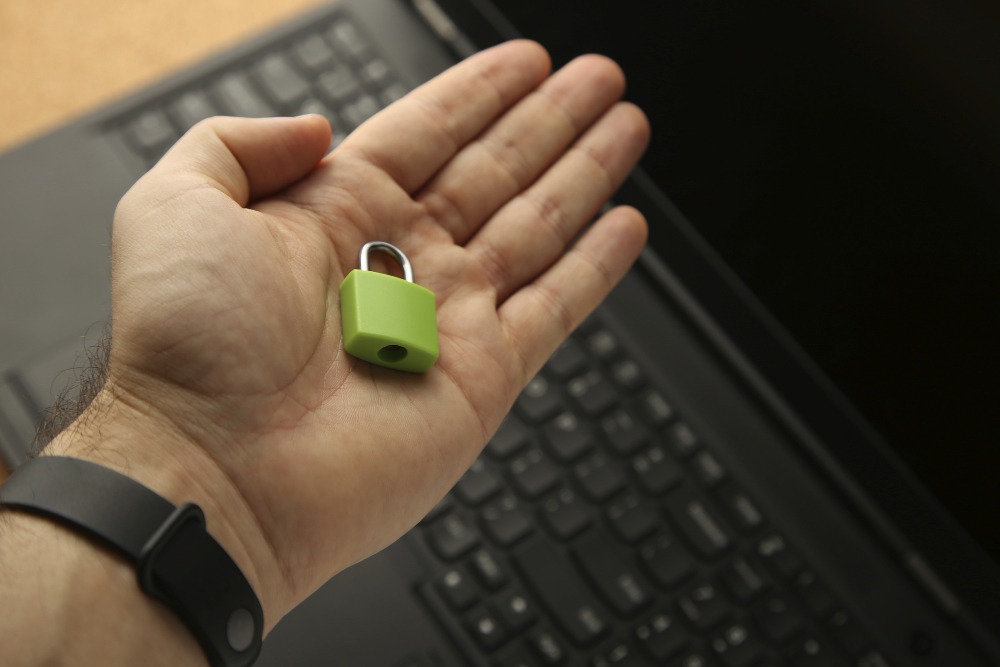 Eine Hand hält ein kleines, grünes Vorhängeschloss über einer Laptop-Tastatur.