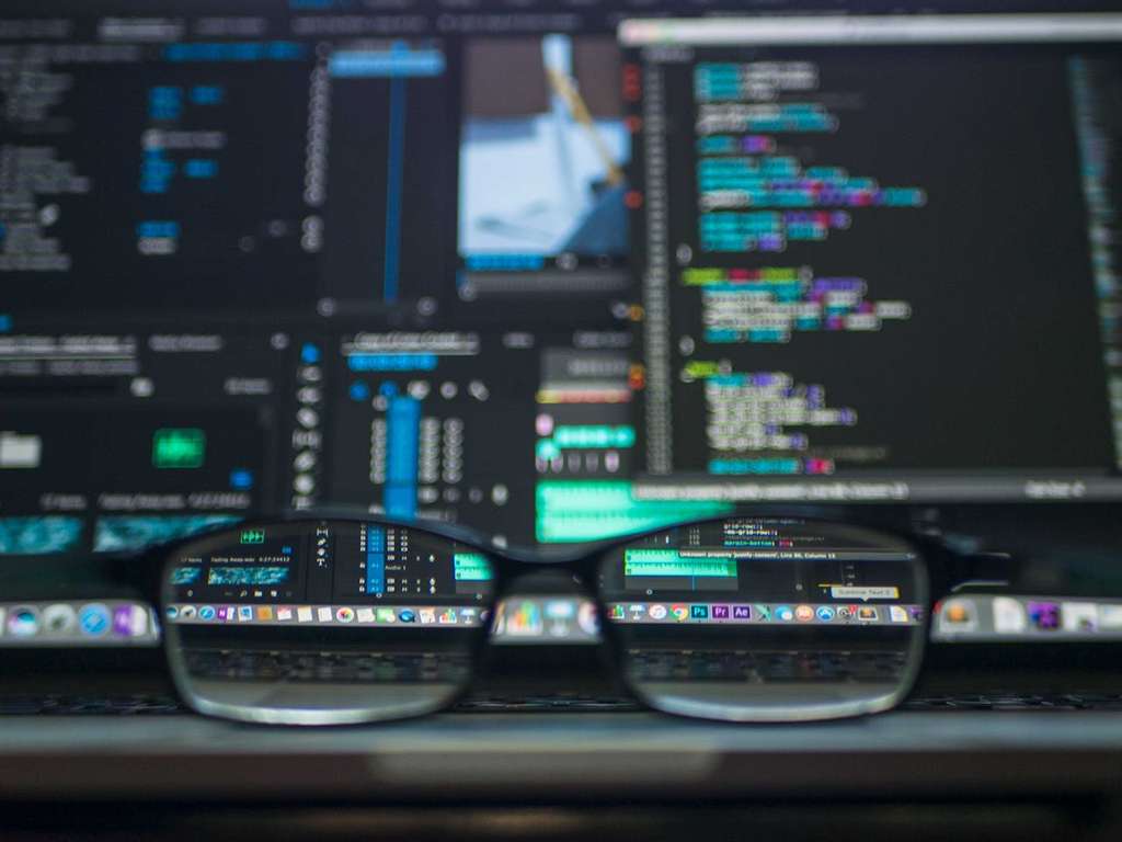 Eine Brille liegt auf einem Laptop, dessen Bildschirm Code in einer dunklen Entwicklungsumgebung anzeigt.
