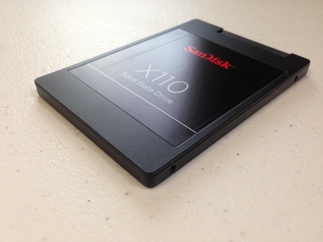 Auf dem Bild ist eine SSD (Solid State Drive) des Herstellers SanDisk zu sehen, Modell X110. Die SSD hat das typische 2,5-Zoll-Format, ist schwarz und liegt leicht schräg auf einer hellen, strukturierten Oberfläche. Auf dem Etikett steht „SanDisk X110 Solid State Drive“.