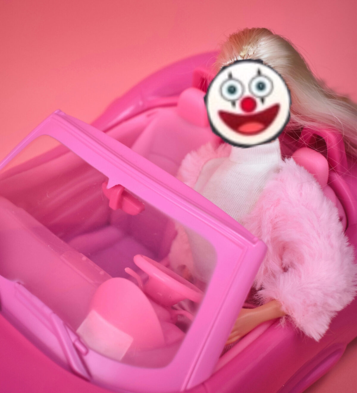 Eine Barbiepuppe sitzt in einem pinken Cabrio – doch ihr Gesicht wurde durch ein Clown-Emoji ersetzt, was die Szene satirisch und absurd wirken lässt. Die Bildkomposition kombiniert knallige Ästhetik mit subtiler Kritik an künstlicher Fröhlichkeit und KI-Spielzeugwahn.